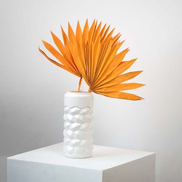 Orange dried palm leaves in white vase placed on coffee table with sofa cushions for boho living room decor.