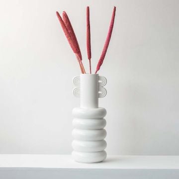 Dried grass stems in red shade styled in white ceramic vase adding artistic accent to modern tabletop home decor.