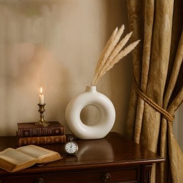 Beige pampas grass stems styled in white donut ceramic vase classic home decor with candle and books.