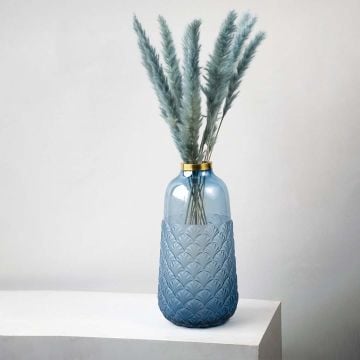 Elegant blue glass vase with pampas grass for modern living room decoration placed on a white pedestal.