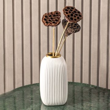 Dried lotus pods styled in elegant white ceramic vase with gold accent placed on green marble table modern lifestyle decor.