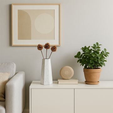 Brown pine cone stems styled in tall marble vase on modern cabinet with green plant and wall art lifestyle home decor.