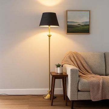 Golden metal floor lamp with black fabric shade styled in modern living room beside beige sofa and wooden table.
