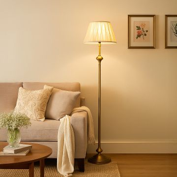 Elegant golden floor lamp with pleated white shade placed beside beige sofa and wooden table in living room.