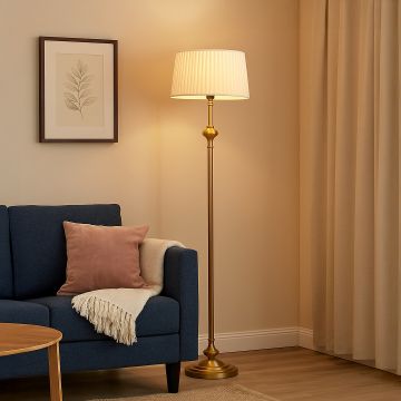 Golden floor lamp with pleated white fabric shade beside navy blue sofa and wall art in cozy living room.