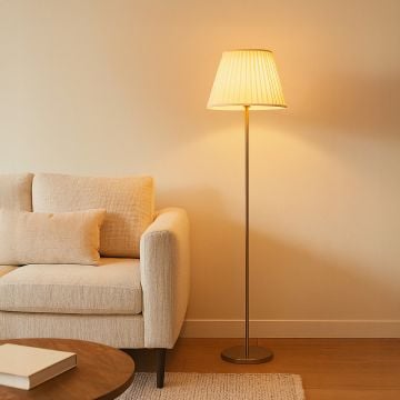 Modern golden floor lamp with pleated white shade styled beside beige sofa in warm living room interior.