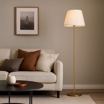 Golden floor lamp with pleated white shade placed beside beige sofa and modern wall art in cozy living room.