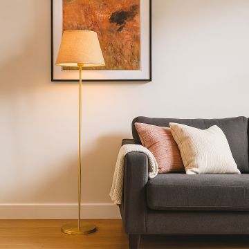 Elegant floor lamp with beige linen shade and golden stand styled in modern living room with grey sofa.