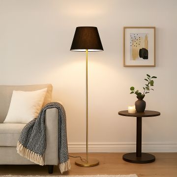 Modern floor lamp with black fabric shade and golden stand placed beside beige sofa in cozy living room.