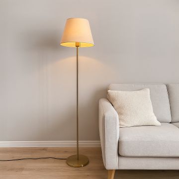 Elegant floor lamp with beige shade and golden stand placed beside a modern grey sofa in a cozy living room.