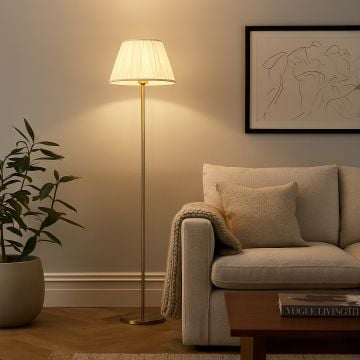 Elegant floor lamp with pleated white fabric shade and gold stand placed beside beige sofa in cozy living room.