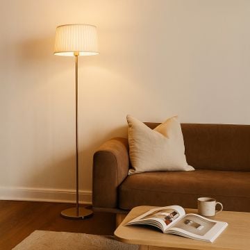 Elegant floor lamp with pleated white fabric shade and gold stand placed beside beige sofa in cozy living room.