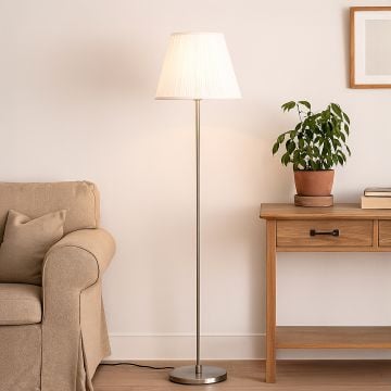 Steel floor lamp with white pleated fabric shade beside beige sofa and wooden table in modern living room.