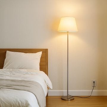 Steel floor lamp with beige fabric shade beside wooden bed in cozy bedroom warm ambient lighting.