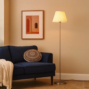 Steel floor lamp with pleated cream shade beside navy sofa and wall art in modern living room lighting decor.