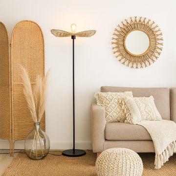 Black floor lamp with rattan leaf shade beside beige sofa in boho living room natural warm interior lighting.