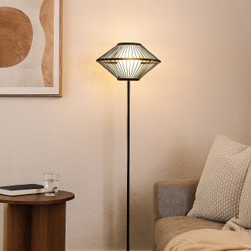 Black floor lamp with geometric wire shade beside beige sofa in modern living room warm cozy lighting.