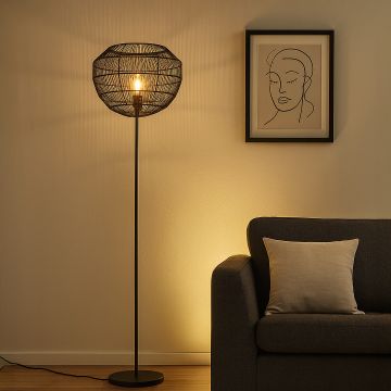 Modern black rattan floor lamp with warm glow placed beside sofa in cozy living room decor.