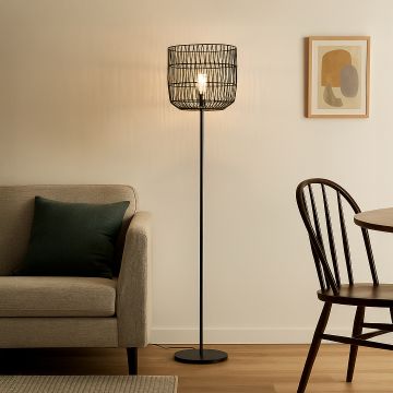 Modern black wire frame floor lamp with warm bulb lighting placed beside sofa in contemporary living room.