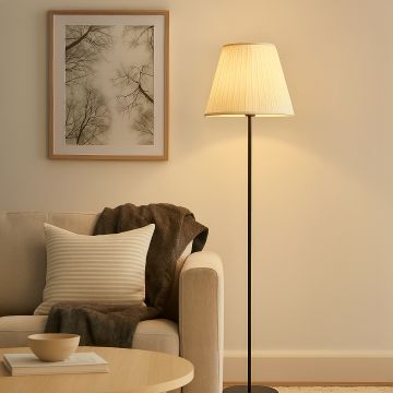 Elegant fabric shade floor lamp with black stand glowing warmly beside beige sofa in cozy living room.