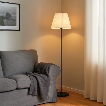 Modern floor lamp with pleated white fabric shade placed beside a grey armchair adding warm ambient lighting to a cozy living room setting with minimalist decor.