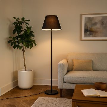 Black floor lamp with fabric shade styled in modern living room beside sofa and indoor plant.