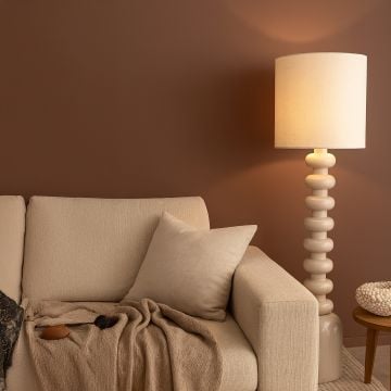 Beige floor lamp placed beside neutral sofa in warm-toned living room creating cozy ambient lighting atmosphere.