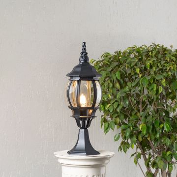 Black outdoor pillar lamp glowing warmly with LED bulb and clear curved glass shade perfect for patio driveway and terrace.