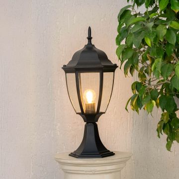Elegant outdoor black pillar light glowing warmly with clear glass shade suitable for entrance patio and landscape use.