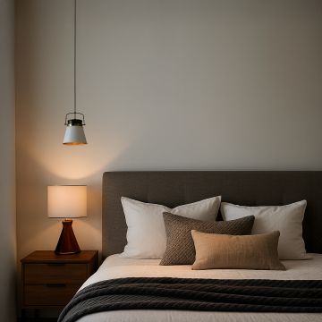 A bedside setup with a white and gold pendant light turned on adding soft illumination to the room with neutral bedding and wood furniture.