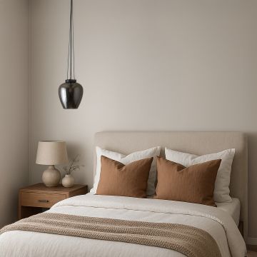 Smoked glass pendant light with black suspension styled above beige bed in modern bedroom interior with warm minimal decor.