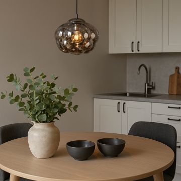 Smokey glass bubble pendant light styled in modern kitchen dining area above round wooden table with ceramic decor.