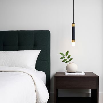 Modern black and gold cylindrical pendant light glowing above bedside table in cozy bedroom interior with soft lighting.