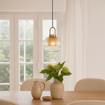 Elegant gold pendant light with ribbed glass shade glowing warmly above dining table styled with ceramic vases and indoor greenery.