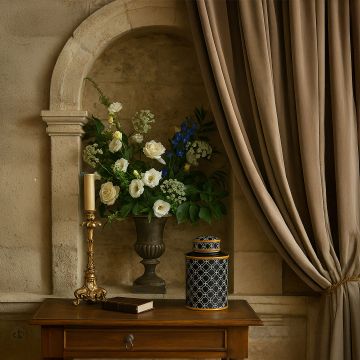 Black patterned jar with gold rim displayed on a wooden table beside flowers and candle adding luxury to interior decor.