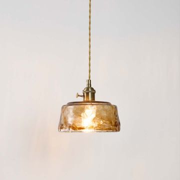 Illuminated amber glass pendant light with brass fixture on white background showcasing vintage industrial farmhouse style.