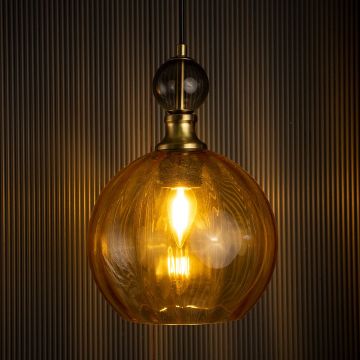 Elegant amber glass pendant light turned on against black background with gold metal accents and spherical design perfect for modern interiors.