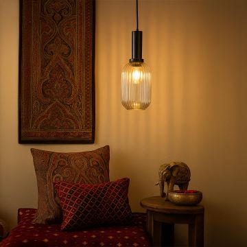 Clear ribbed glass pendant light with black holder glowing warmly in a cozy room with ethnic decor.