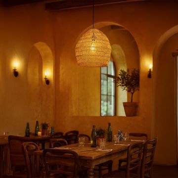 Open weave rattan pendant light in natural bamboo finish glowing warmly above dining table in rustic home decor.