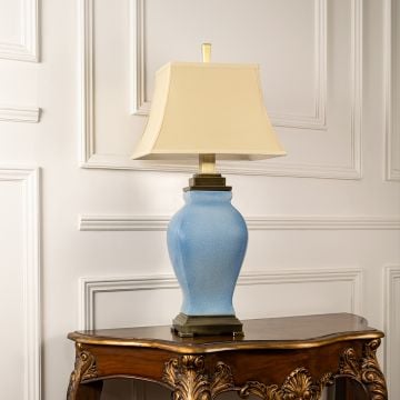Cream shade blue ceramic table lamp on carved console table with light on and white panel wall background for classic elegant décor.