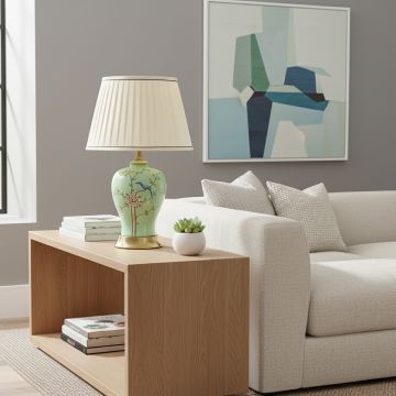 Green ceramic table lamp with hand painted floral bird design brass base and fabric shade styled on bedside or living room table.