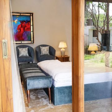 Ceramic table lamp glowing beside a cozy bed with blue velvet seating soft cushions and vibrant wall art in a modern bedroom setting.