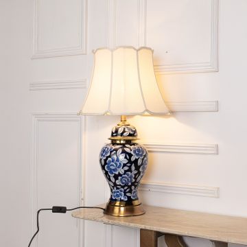 Blue floral ceramic table lamp with gold base and cream fabric shade casts a warm soft light creating a serene and sophisticated ambience.