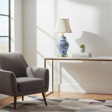 Blue and white ceramic table lamp with traditional floral pattern brass base and fabric shade styled in living room corner.