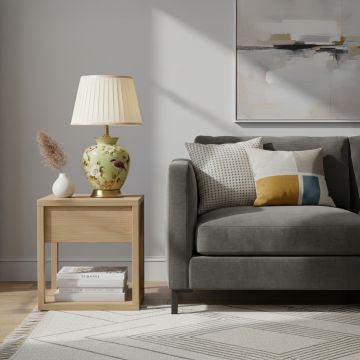 Green ceramic table lamp with hand painted bird and floral artwork brass base and pleated fabric shade styled on side table.