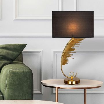 Gold artistic table lamp with black shade styled beside a green sofa on a round table creating a warm inviting glow in a contemporary home interior.