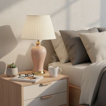 Blush pink ceramic table lamp with textured glazed body gold metal base and pleated fabric shade styled on bedside table.