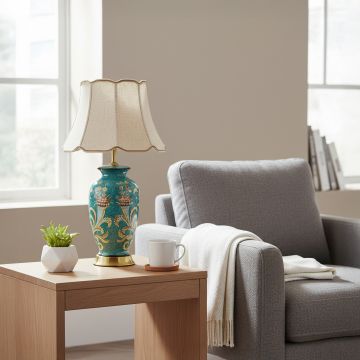 Teal ceramic table lamp with ornate floral artwork gold metal base and fabric shade styled on elegant living room side table.