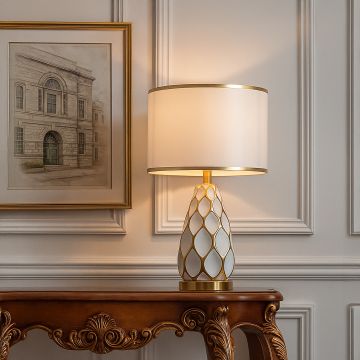 Gold ceramic table lamp with white shade glowing beside sofa for modern living room and bedroom interior lighting.