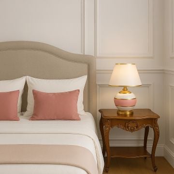 Pink ceramic table lamp with gold accents and white shade glowing on bedside table for elegant bedroom lighting decor.